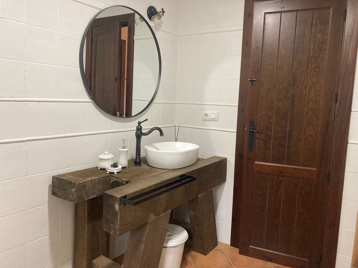 Primer baño: lavabo sobre encimera de madera y espejo redondo