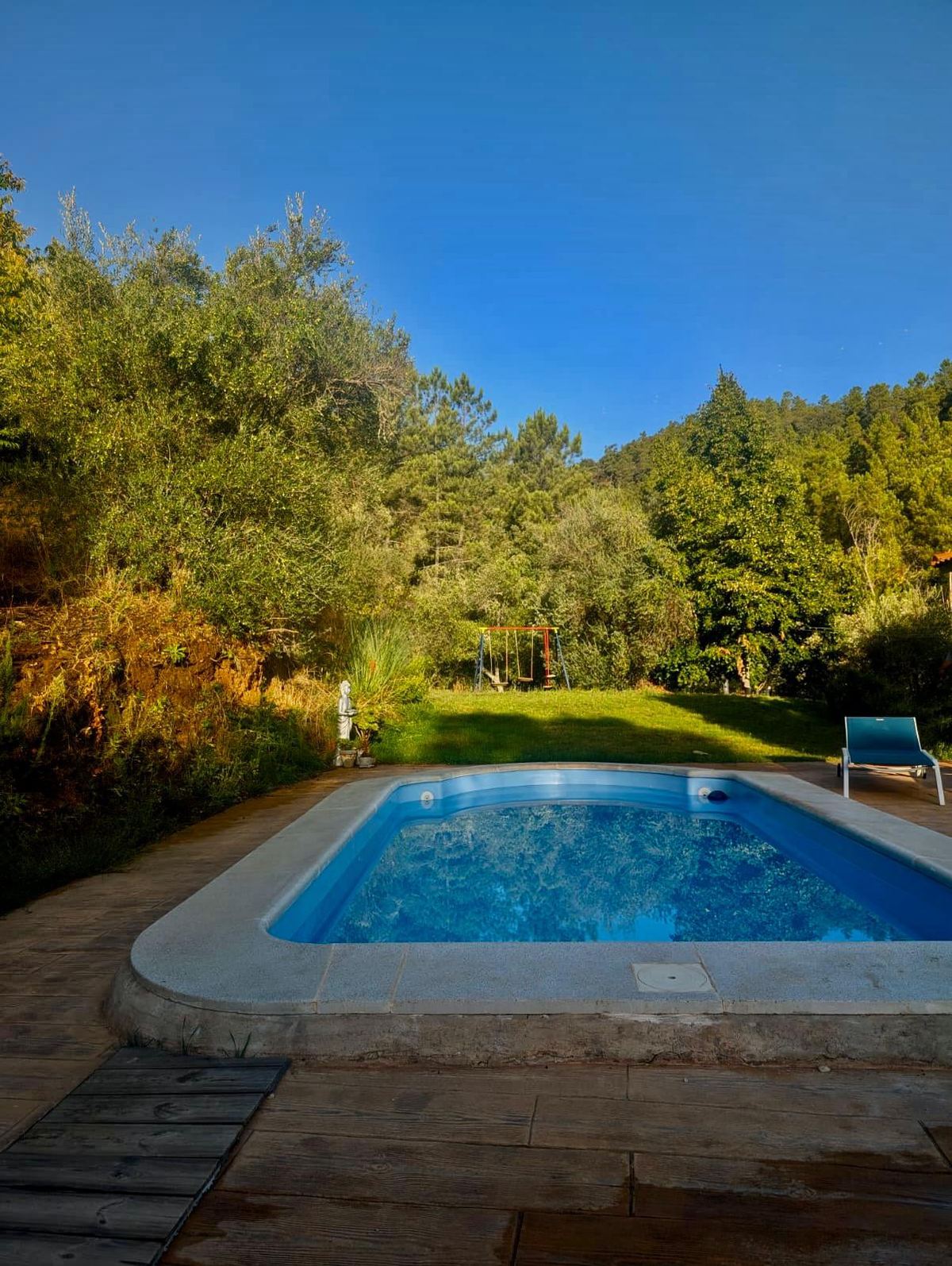 Piscina privada rodeada de césped, con tumbona a la sombra